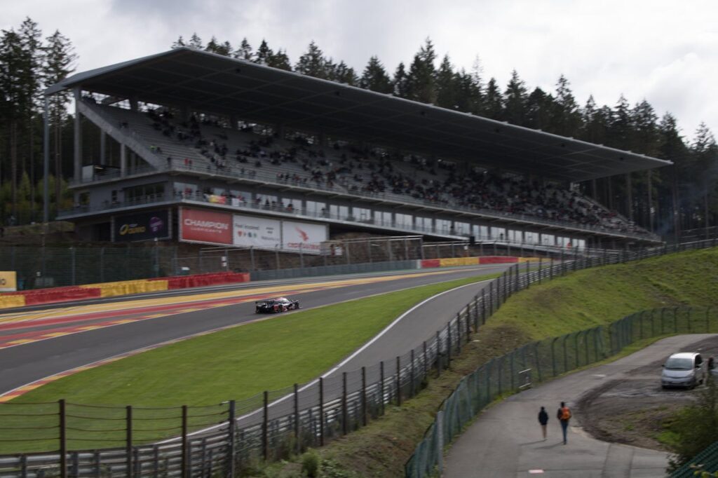 An F1 car drives in front of a stand of fans at the Spa-Francorchamps circuit. Are you going to the next F1 race in Belgium?